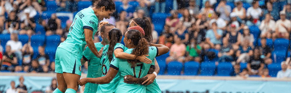KC Current players in teal huddling to celebrate a goal scored by Michelle Cooper