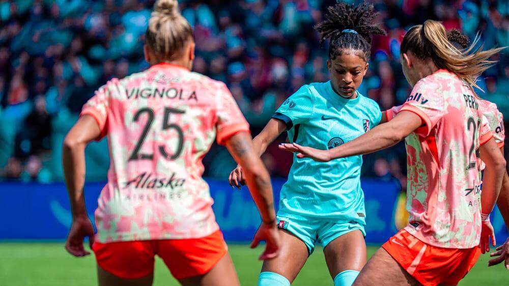 Croix Bethune facing Portland Thorns defenders in her teal uniform.
